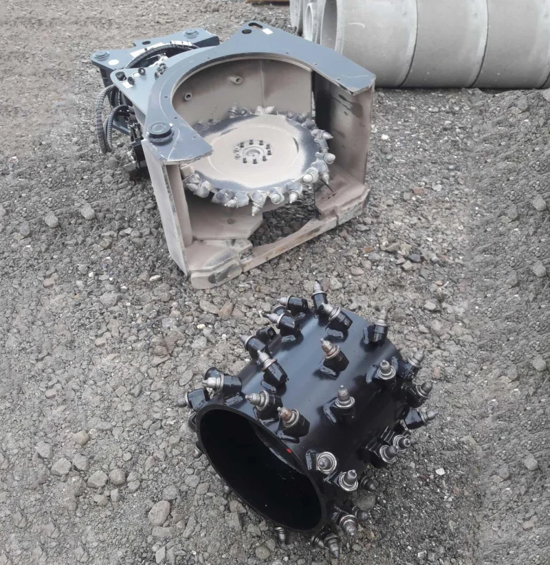 Ein Flächenfräse mit Fräsrad und eine separate Frästrommel liegen auf einem Schotterplatz. Die auswechselbaren Werkzeuge ermöglichen das Fräsen sowohl von Flächen als auch von schmalen Schlitzen mit demselben Anbaugerät